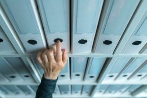 A person's hand reaches to take a blue file folder from a row of similar folders on shelves, highlighting the meticulous organization integral to our services.