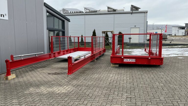 Zwei rote Industrieplattformen mit Sicherheitsgeländern stehen im Freien auf einem gepflasterten Platz in der Nähe eines Gebäudes. Eine Plattform mit der Aufschrift „ALPRO“ präsentiert stolz ihre robusten Produkte. Im Hintergrund sind Schneeflecken zu sehen, die der Kulisse einen Hauch von Winter verleihen.