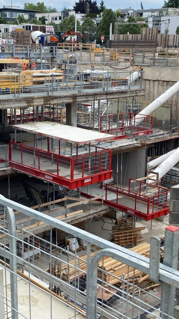 Construction site with multiple red work platforms suspended in place, scaffolding, wood planks, and concrete structures in progress—solutions for every job and every size.